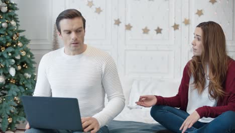 Aggressive-young-woman-hindering-man-working-on-computer-on-remote-workplace.