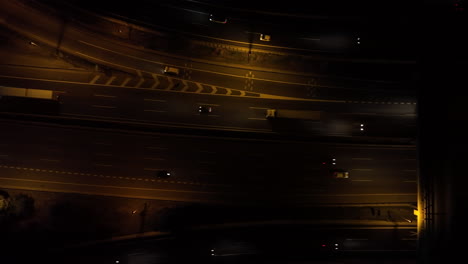 Illuminated-traffic-headlights-driving-along-busy-highway-at-night,-aerial-Birdseye-view