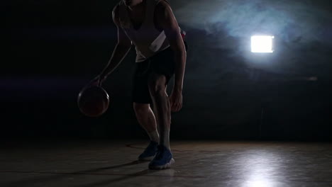 one-young-adult-man,-basketball-player-dribble-ball,-dark-indoors-basketball-court.-Smoke-slow-motion
