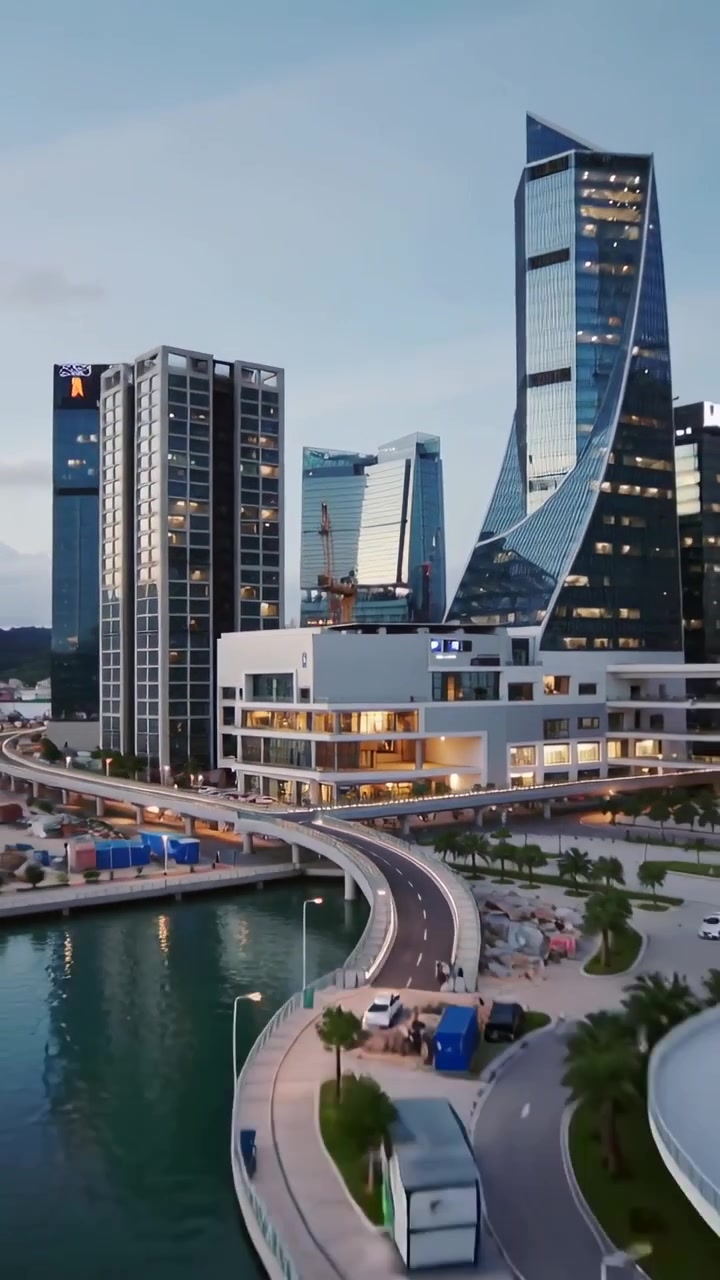 Vertical video: Pulling back camera revealing white building at dusk harbor, showing crane, skyline