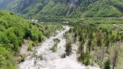 vista de aviones no tripulados en albania en los alpes ascendiendo en un valle verde con un río de suelo rocoso con agua cristalina en el