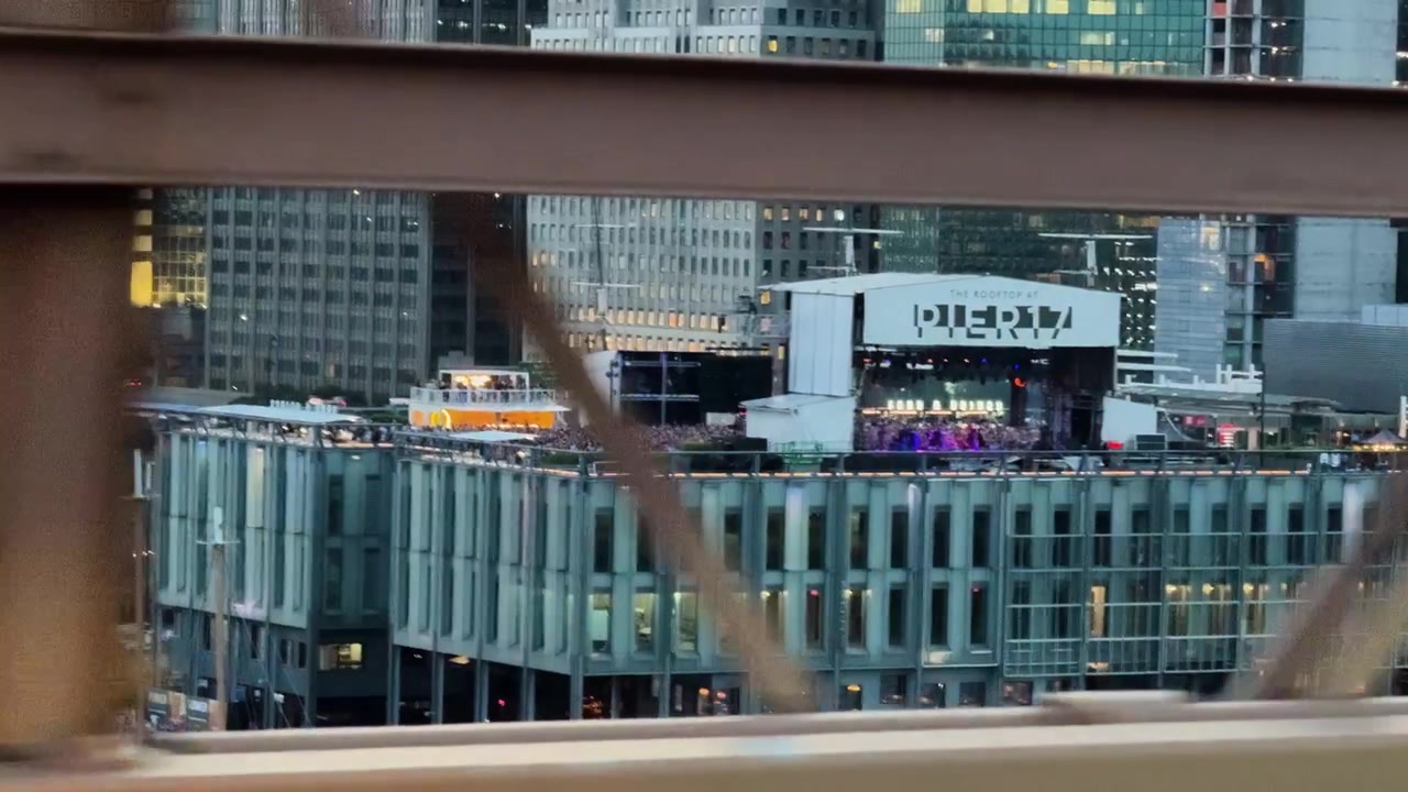 Vista di un evento sul tetto al Molo 17 attraverso la struttura del Ponte di Brooklyn al tramonto