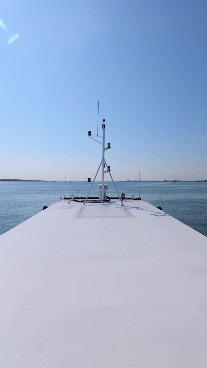 Hochwertige 60fps Zeitlupenaufnahme im Hochformat (9:16) eines Schiffes, das sich durch ruhiges Wasser bewegt, wobei die Symmetrie des Schiffes und die entfernte Küstenlandschaft betont werden.