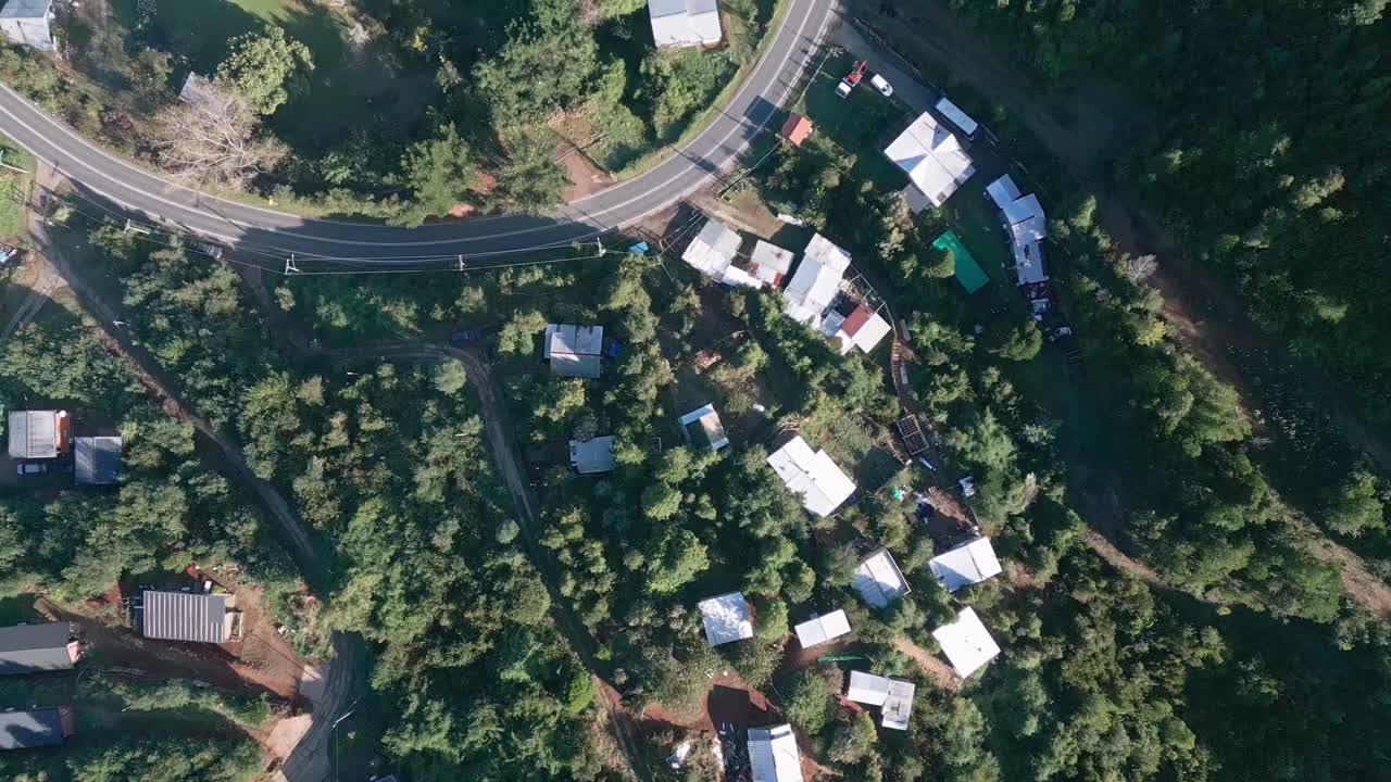 Top-down bird's eye drone aerial of Niebla village with scattered houses, colorful rooftops, curved roads, and dense forest vegetation