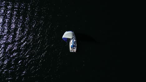 From-an-aerial-perspective,-a-sailboat-gracefully-appears-with-its-vibrant-sail,-gliding-on-the-dark-waters-of-the-Baltic-Sea