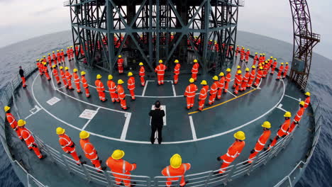 workers in orange jumpsuits gather in formation on an offshore platform