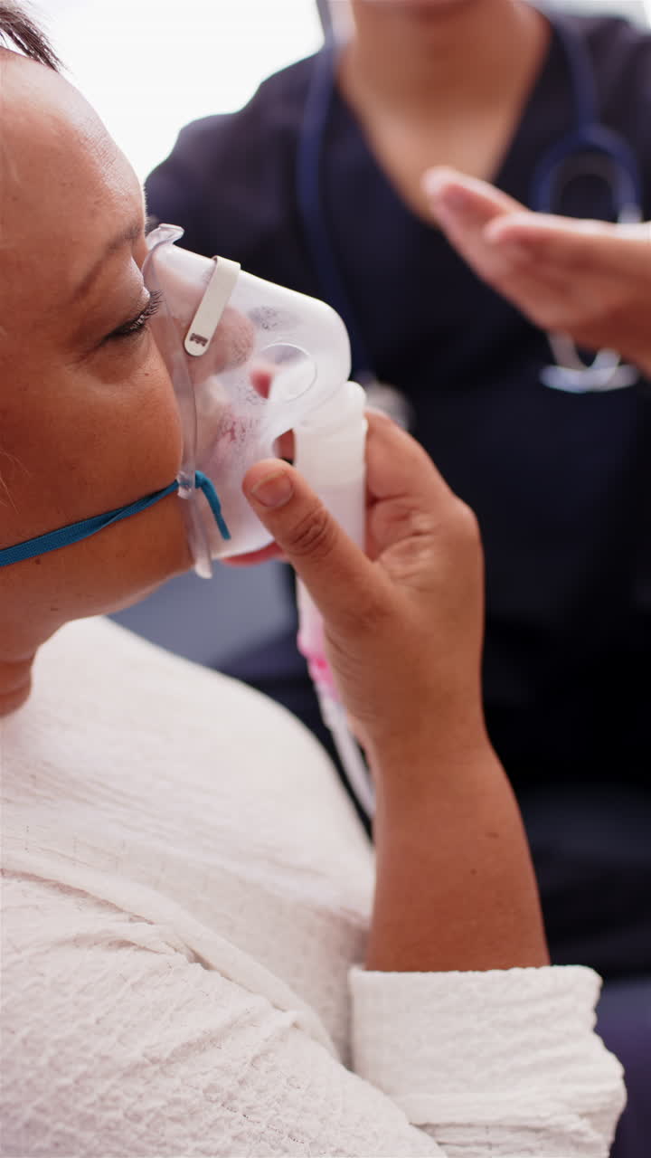 Vertical video: Using oxygen mask, senior woman receiving respiratory therapy from male physiotherap