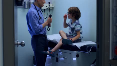 Side-view-of-young-asian-male-doctor-examining-a-caucasian-boy-patient-eye-with-tool-in-a-clinic-4k