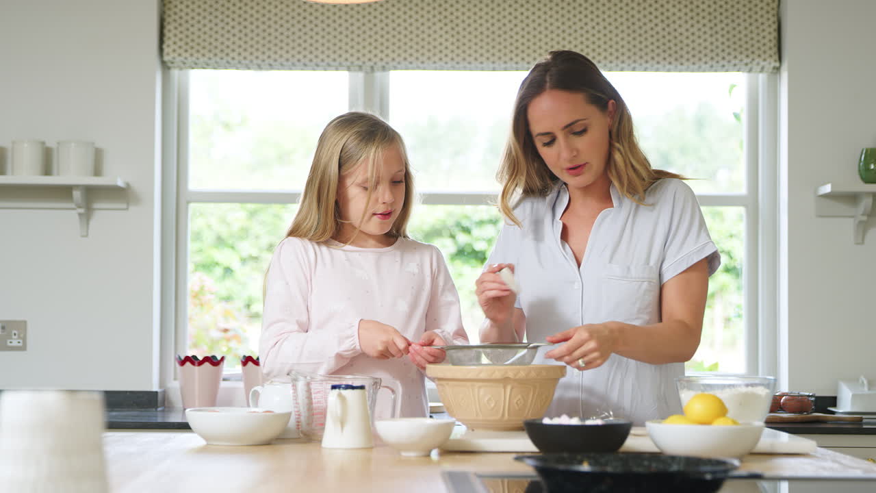 피자마를 입은 어머니와 딸이 함께 집에서 주방에서 팬케이크를  ⁇ 고 만들고 있습니다.
