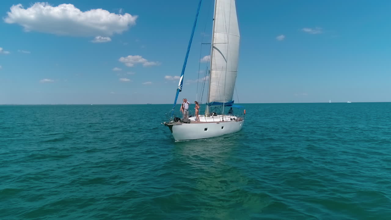 Young people rest on a yacht in summer. Male singer and two girls dancing on a sailboat on blue sea background. Joyful summer sea voyage.