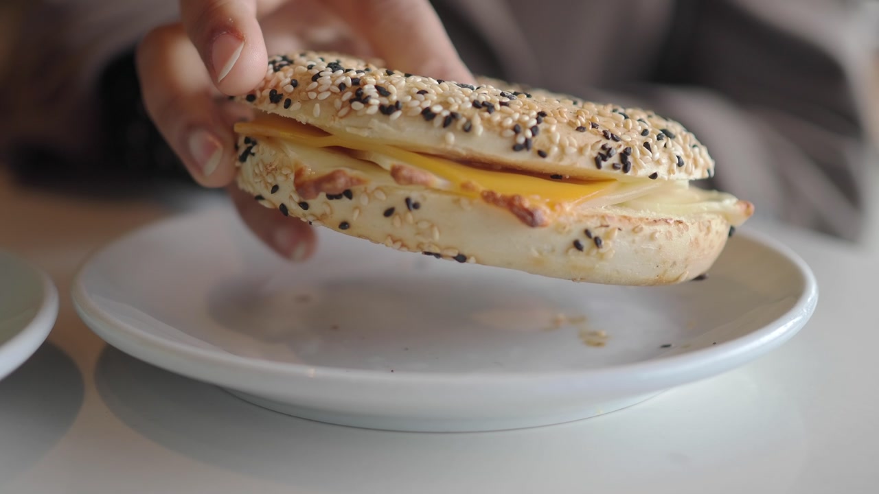 Close-up of a Hand Picking Up a Cheese Bagel Sandwich