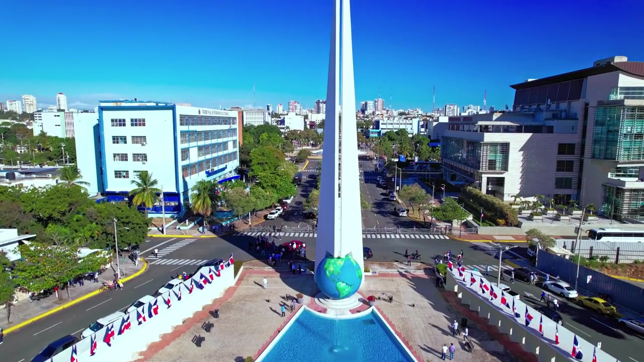 Ripresa aerea diurna con drone che vola in avanti e sale attraverso un pergolato per rivelare il monumento La Bolita del Mundo e viale Jimenez Moya a Santo Domingo, Repubblica Dominicana
