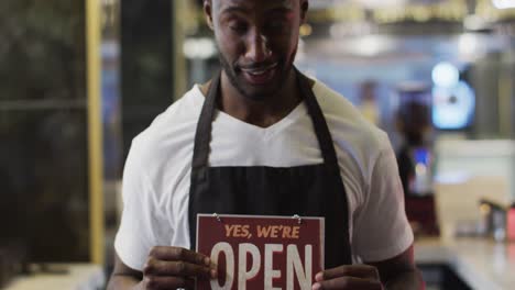 Portrait of happy african american barista holding &#039;we&#039;re open&#039; sign in cafe