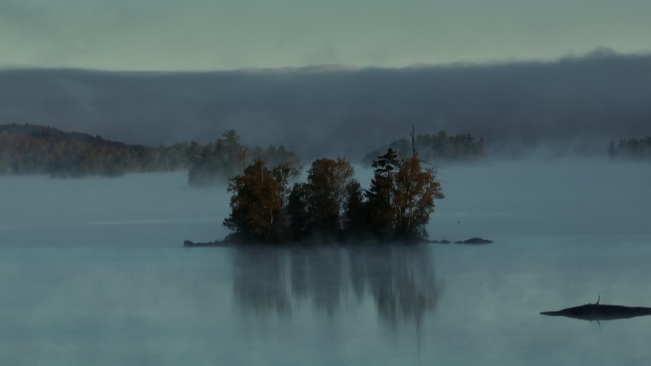 Aerial view of fog sets in around lone island on lake Slow-Motion