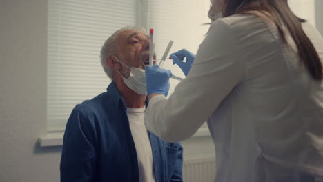 hombre anciano dando pruebas de saliva en la clínica de cerca. mujer médico tomando muestra.