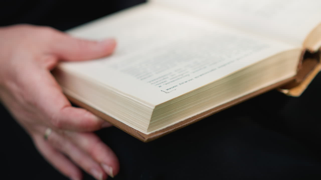 Close up partial view of lady flipping through old book pages carefully while reading outdoors, fingers turning paper slowly in calm relaxed motion, symbolizing curiosity