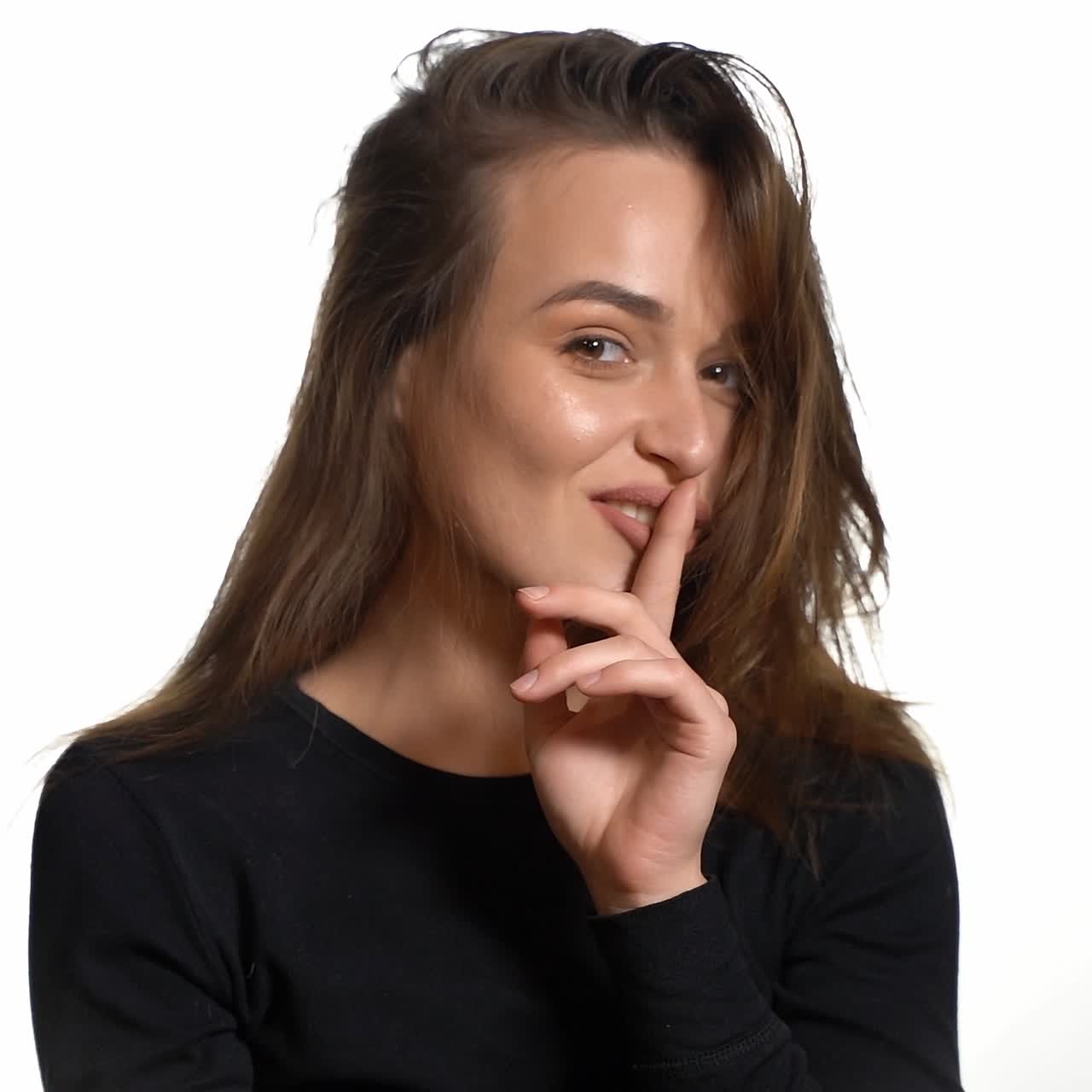 A gorgeous girl in a black jumper is throwing back her hair and smiling on a white background in the studio. Close-up