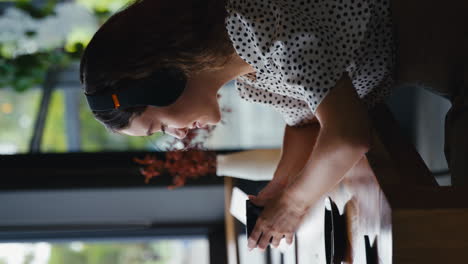 Vertical-Video-Of-Businesswoman-Wearing-Wireless-Headphones-Working-On-Laptop-Drinking-Coffee