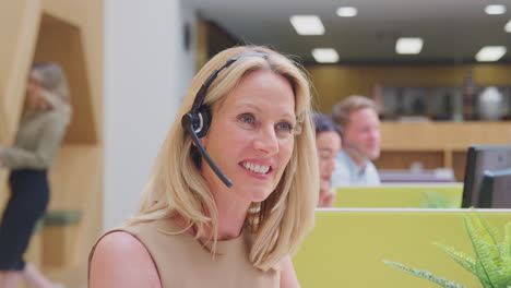 portrait of mature businesswoman wearing headset talking to caller in customer services centre
