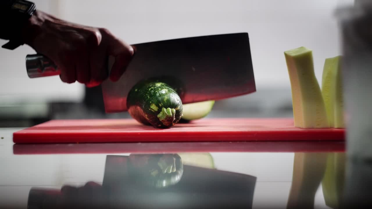 Unique view in slow motion of a chef with a butcher knife cutting a zucchini in half.