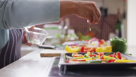 Mid-section-of-asian-senior-woman-sprinkling-herbs-over-vegetable-salad