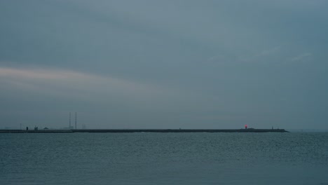Dublin Bay at dusk with Poolbeg Towers and East Pier Lighthouse visible in the distance. The calm sea reflects the soft blue hues of the sky.