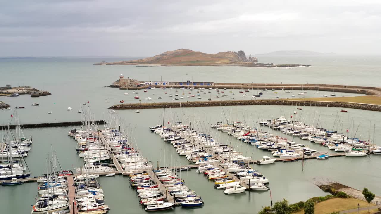 Drone trucking pan above boats docked in harbor with Ireland's Eye in backdrop