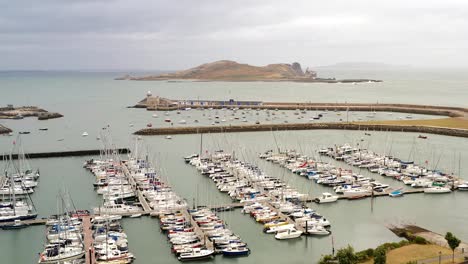 drone trucking pan above boats docked in harbor with ireland's eye in backdrop