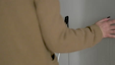 woman in brown coat touching the wall and picking up a walking stick before leaving home