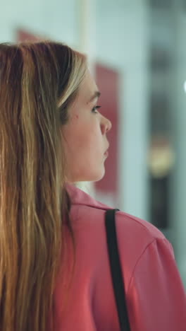 dama de vestido rosa caminando por un centro comercial, mirando hacia atrás por encima de su hombro, los reflejos de la gente y las luces del centro comercial son visibles en las ventanas de vidrio por el lado