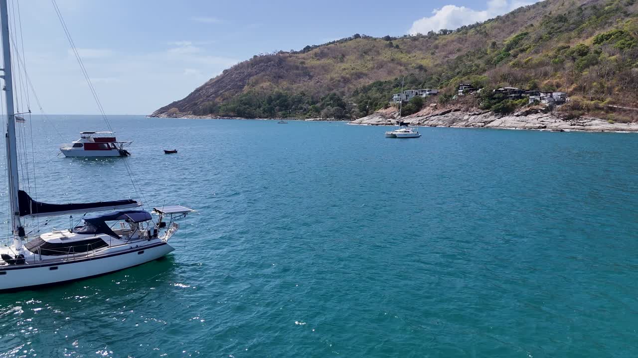 Drone footage captures boats sailing in a serene bay in Phuket, Thailand, showcasing clear waters and lush hillsides
