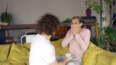 joyful man making marriage proposal to his boyfriend, hugging together on a sofa in living room