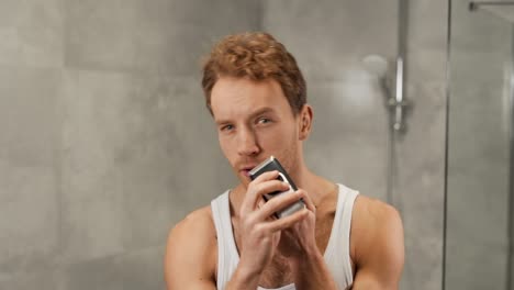 handsome sporty man in t-shirt shaves with electronic razor shaver