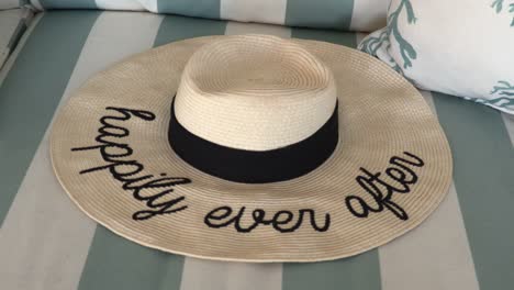 happily ever after straw hat laying on a striped couch at a beach house