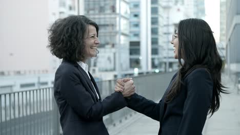 two smiling women meeting on street and shaking hands