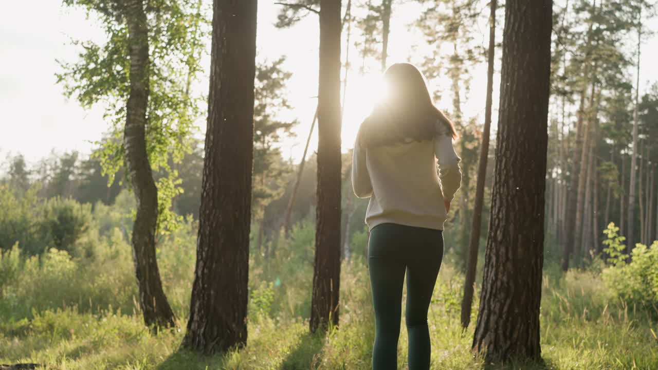 해가 지는 동안 나무 사이에서 잔디 위에서 조하는 여성. 여성 달리기 선수는 저녁에 울창한 숲의 멋진 전망과 함께 심장 운동을 즐긴다. 자연에서 혼자 운동