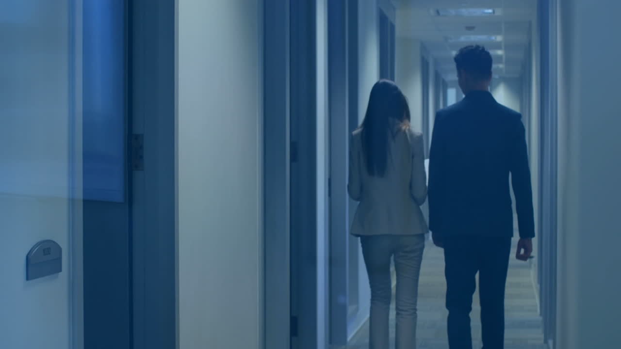 Walking in dimly lit hallway, two people in office building discussing animation