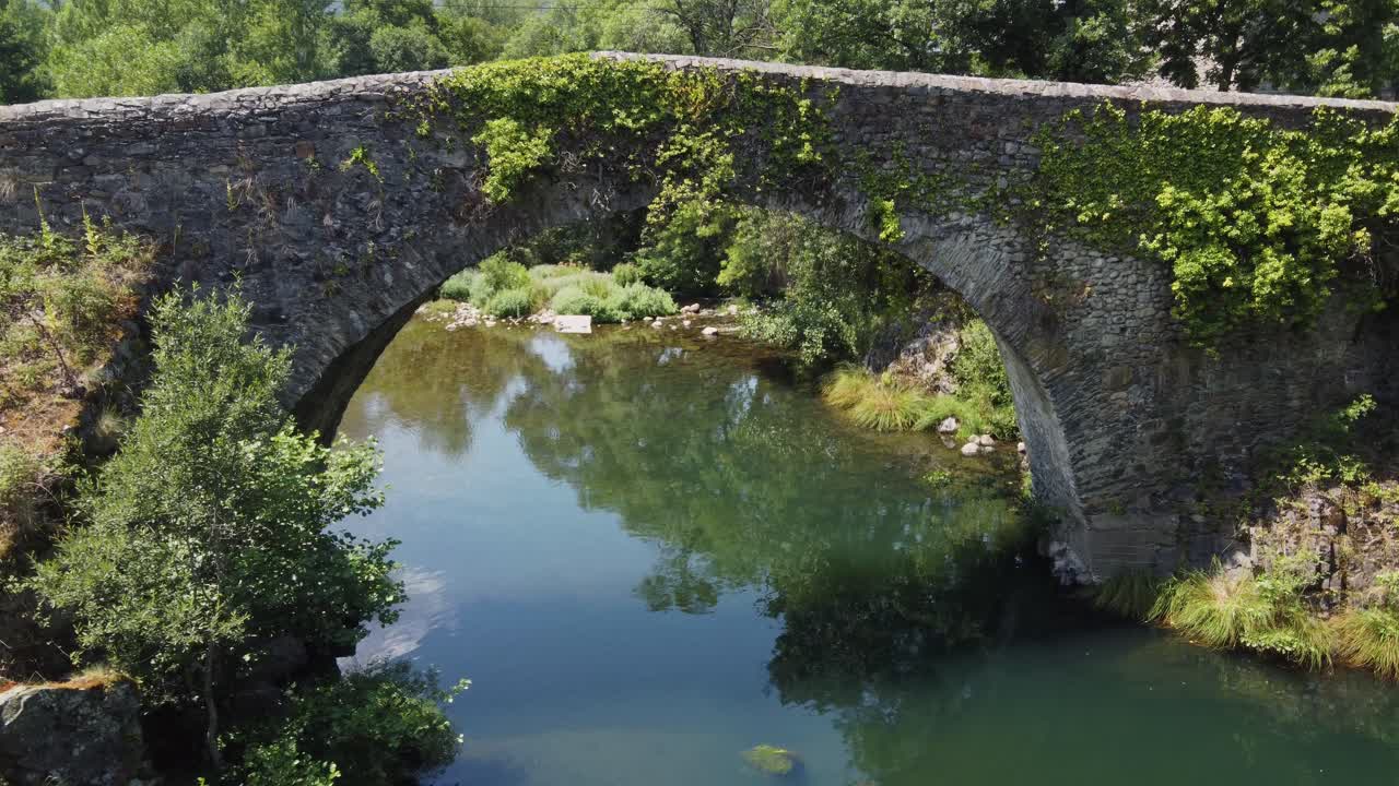un antiguo puente romano en la españa rural sobre un río - vuelo de drones bajo el puente