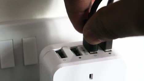 close up view of hand plugging 2 usb cables into white 4 port usb charger indoors