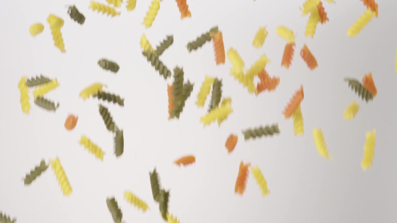 Dry uncooked Colored Fusilli Rogini raining down on a white backdrop in slow motion close up macro.