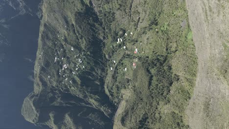 Vertikales,-Unbearbeitetes-4K-Video-Von-Drohnenaufnahmen-In-Einem-Großen-Krater-Mit-Kleinen-Häusern-Und-Einem-Riesigen-Berg,-Der-Kurz-Nach-Sonnenaufgang-In-Sicht-Kommt