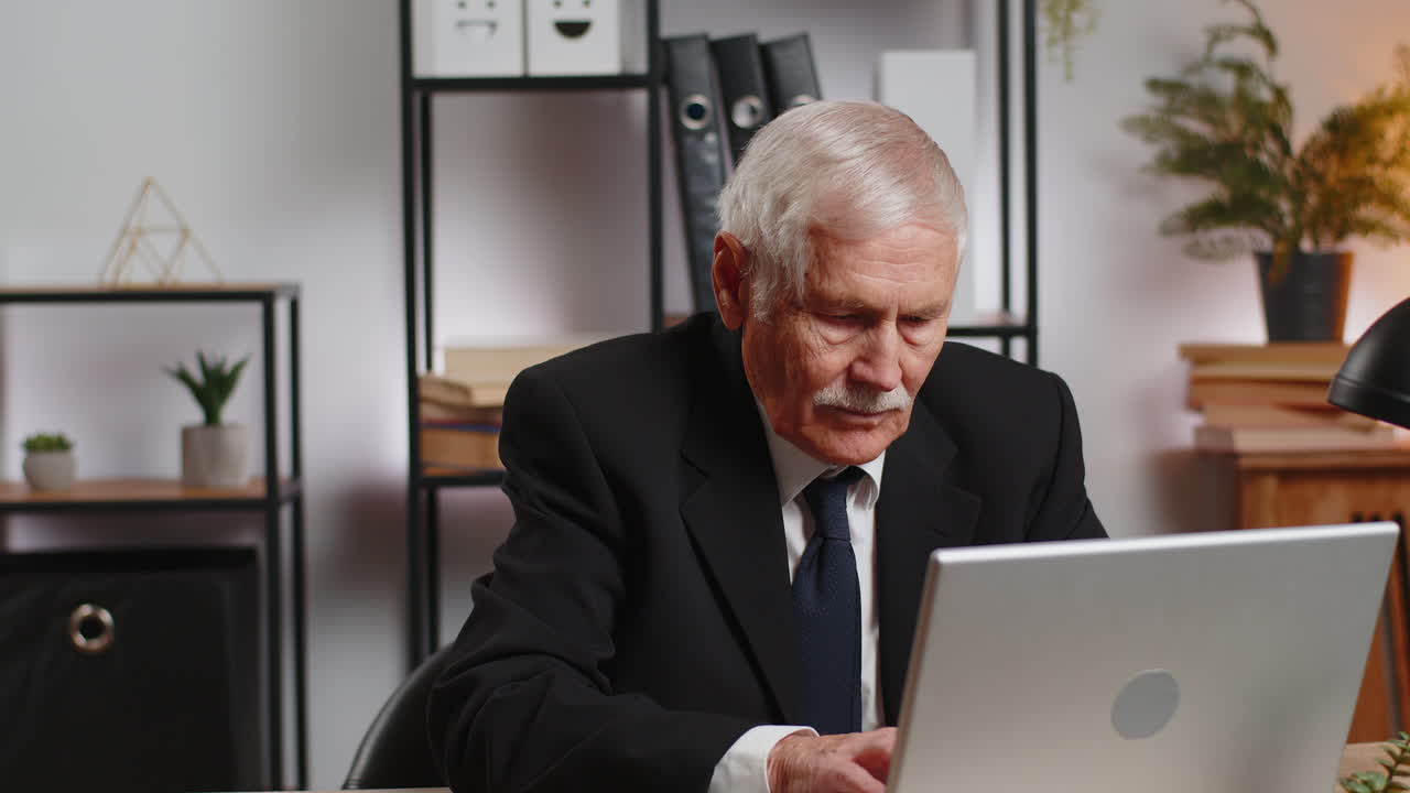 Nonno caucasico, uomo d'affari, seduto alla scrivania dell'ufficio di casa che chiude il PC portatile dopo aver finito di lavorare