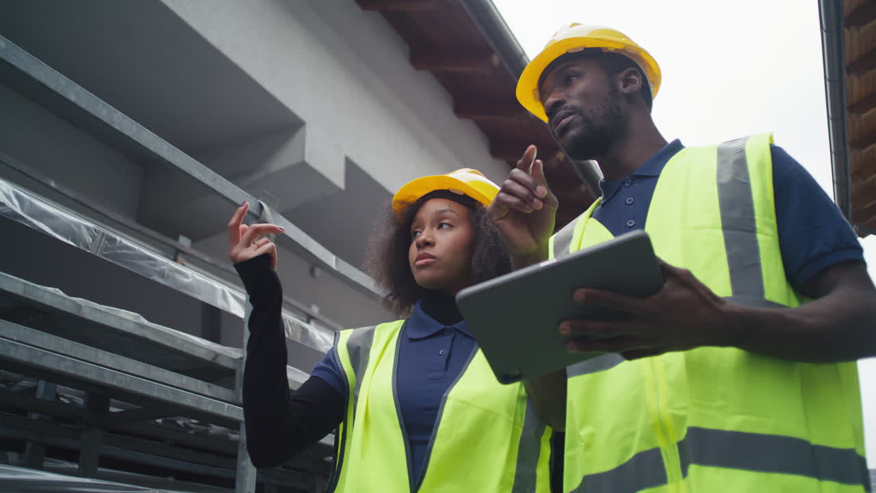 Two workers wearing protective gear yellow hard hats and safety vests taking inventory in an outdoor