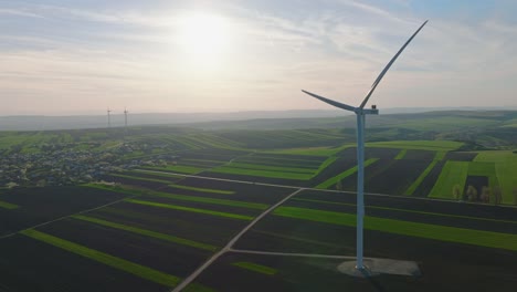 Wind-turbine-stands-tall-over-vast-green-and-black-patchwork-fields-under-a-bright-sunny-sky