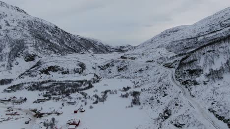 Drone-view-in-Tromso-area-in-winter-flying-over-a-snowy-landscape-with-wooden-houses-and-white-mountains-in-Norway