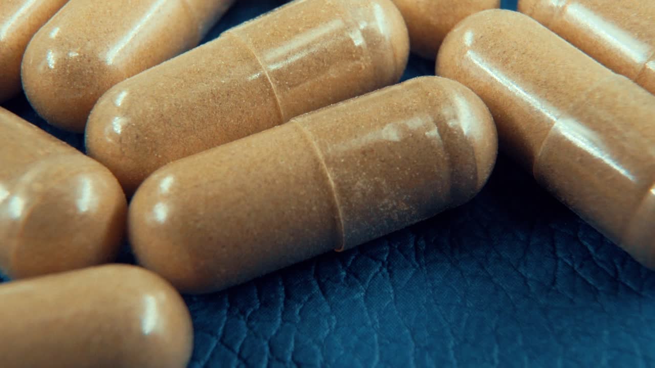 una cámara lenta macro cinematográfica tomada en un laboratorio de una cápsula médica con polvo, píldoras orgánicas, en un patrón azul, luz de estudio, 120 fps, full hd