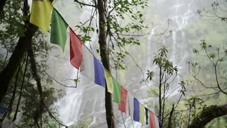 colourful prayer flags in nature in nepal, colorful buddhist prayer flags and waterfall in a forest in the himalayas on the annapurna circuit trekking route