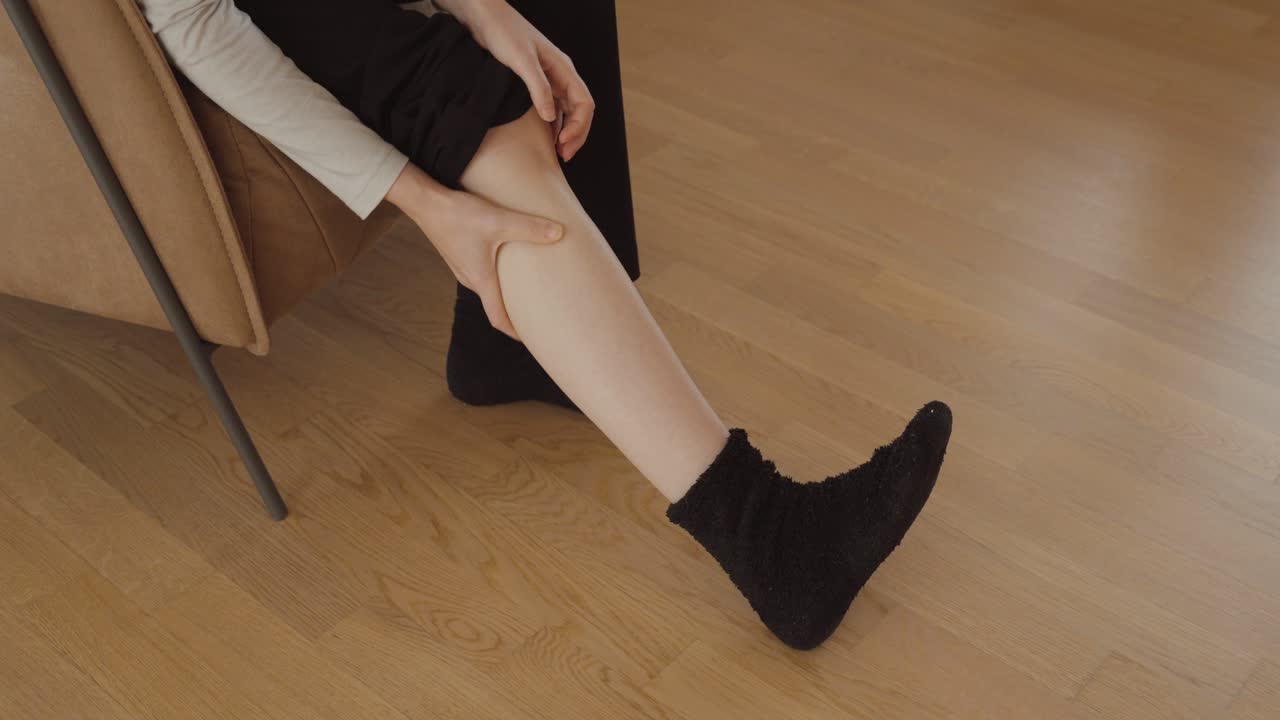 Primo piano di una donna seduta che massaggia il polpaccio per alleviare i crampi muscolari o il dolore alle gambe: concetto di rimedio casalingo e rilassamento