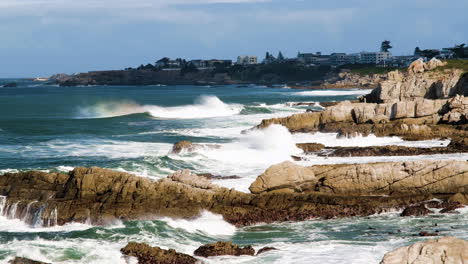 strong wind blows spray off top of waves rolling toward rocky shore, hermanus