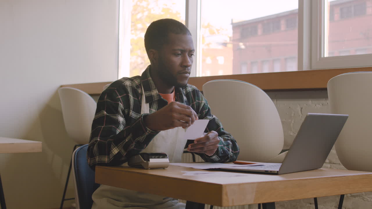 Coffee Shop Owner Sitting At Table And Calculating Finance Bill On Laptop Computer